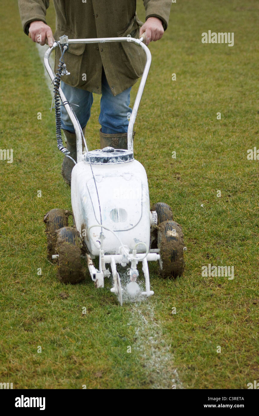 Groundsman painting white lines on football pitch using a push along