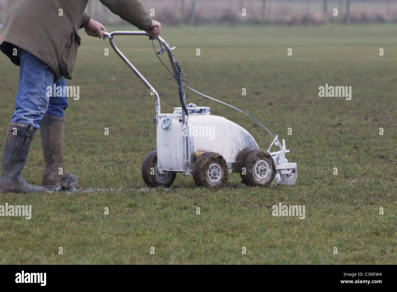 Groundsman painting white lines on football pitch using a push along machine Stock Photo