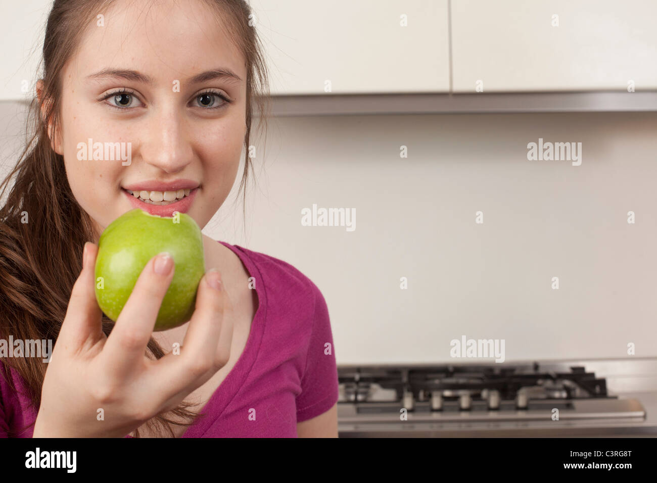 teenage girl eating an apple in kitchen Stock Photo