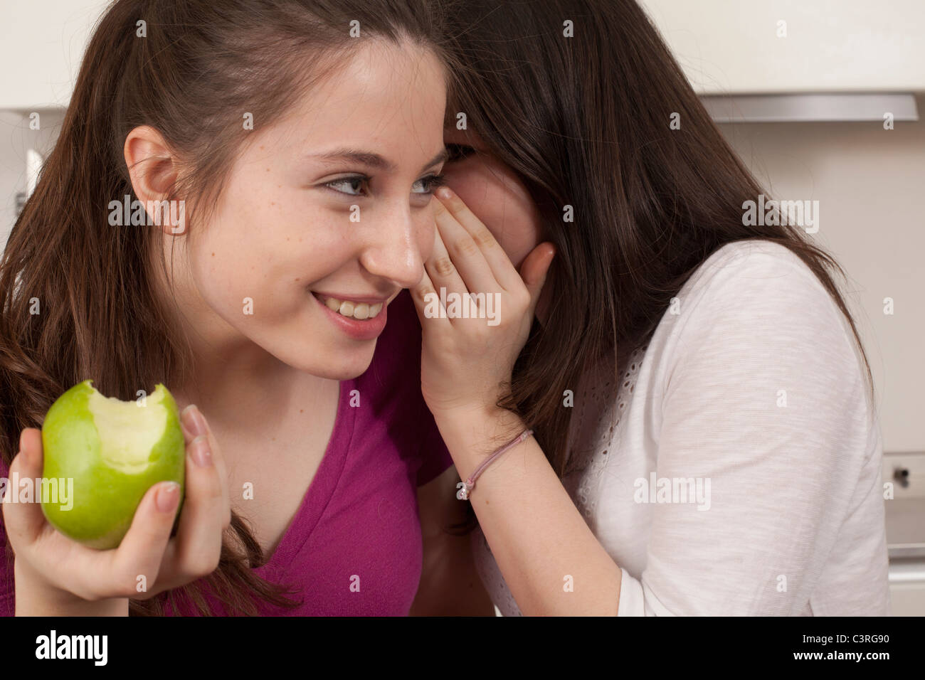teenage girls eating an apple and sharing a secret Stock Photo