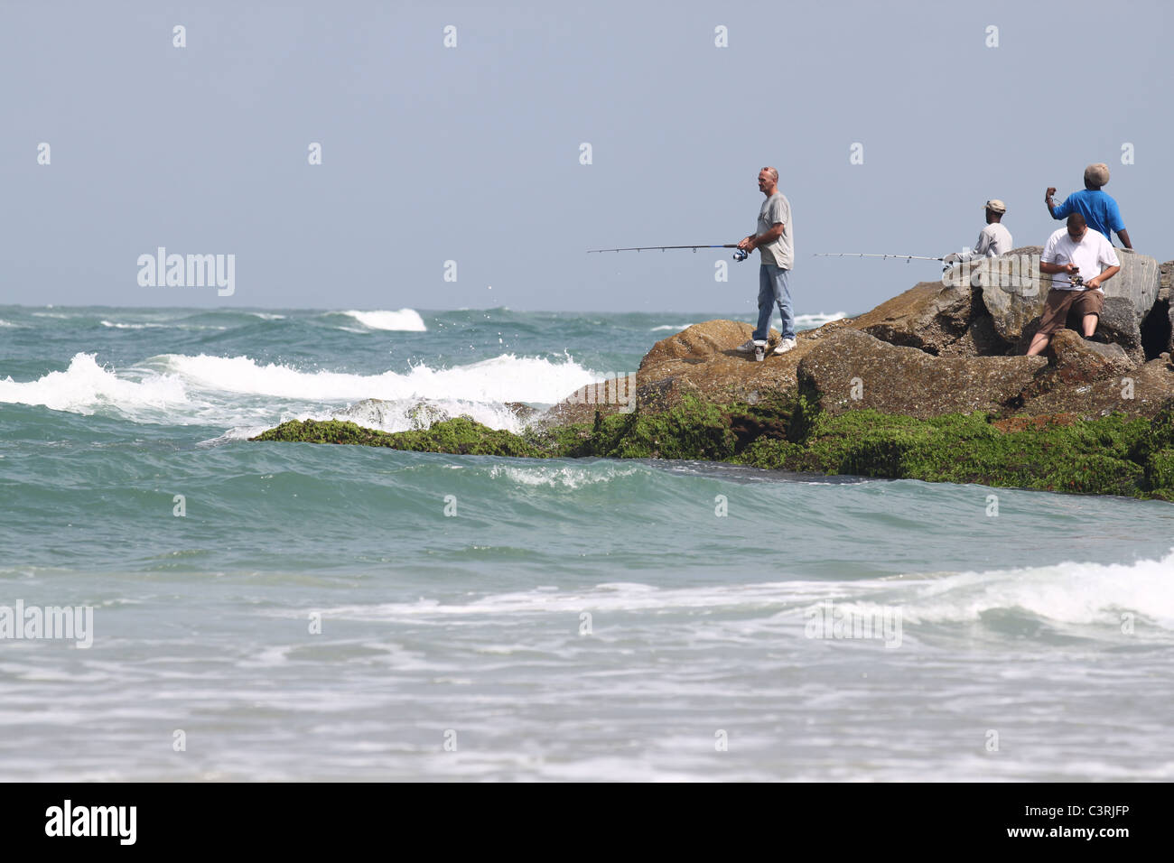 Four men fishing off a natural pier at Smyrna beach, Florida Stock Photo
