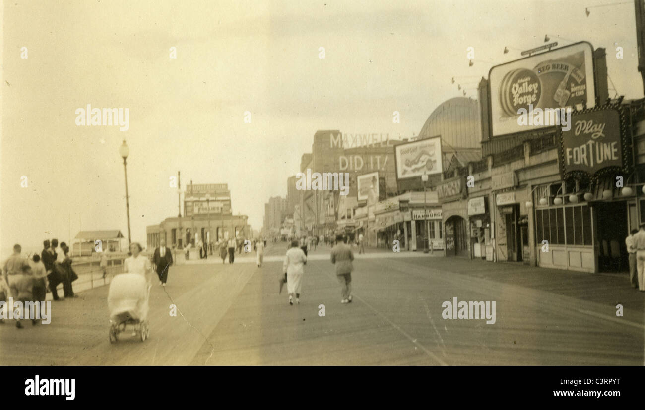 Tourists walking on Atlantic City New Jersey boardwalk during 1930s Maxwell Did It! billboard advertisements wood beach ocean to Stock Photo