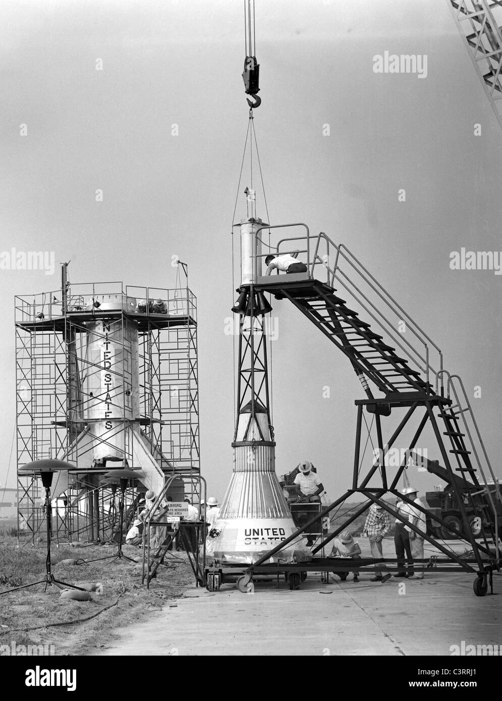 Technicians adjust the rocket motor during attachment of the escape tower to Mercury capsule prior to assembly with Little Joe Stock Photo