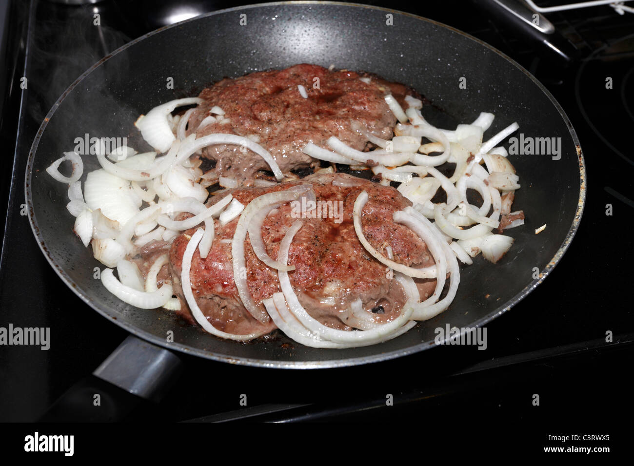 Raw hamburger patties with onions in Teflon coated skillet Stock Photo