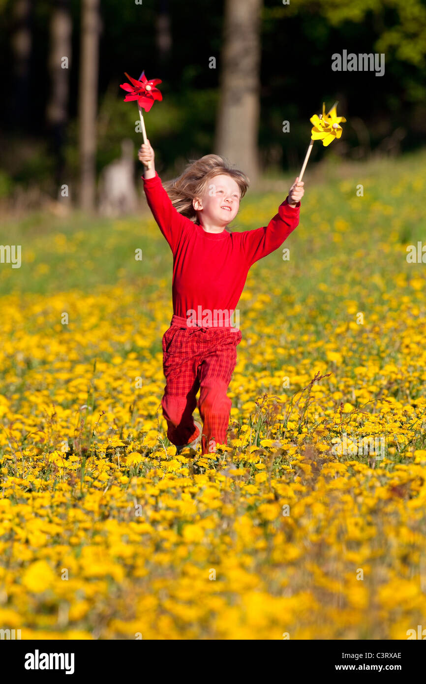 boy with long blond hair playing with pinwheels on a dandelion meadow ...
