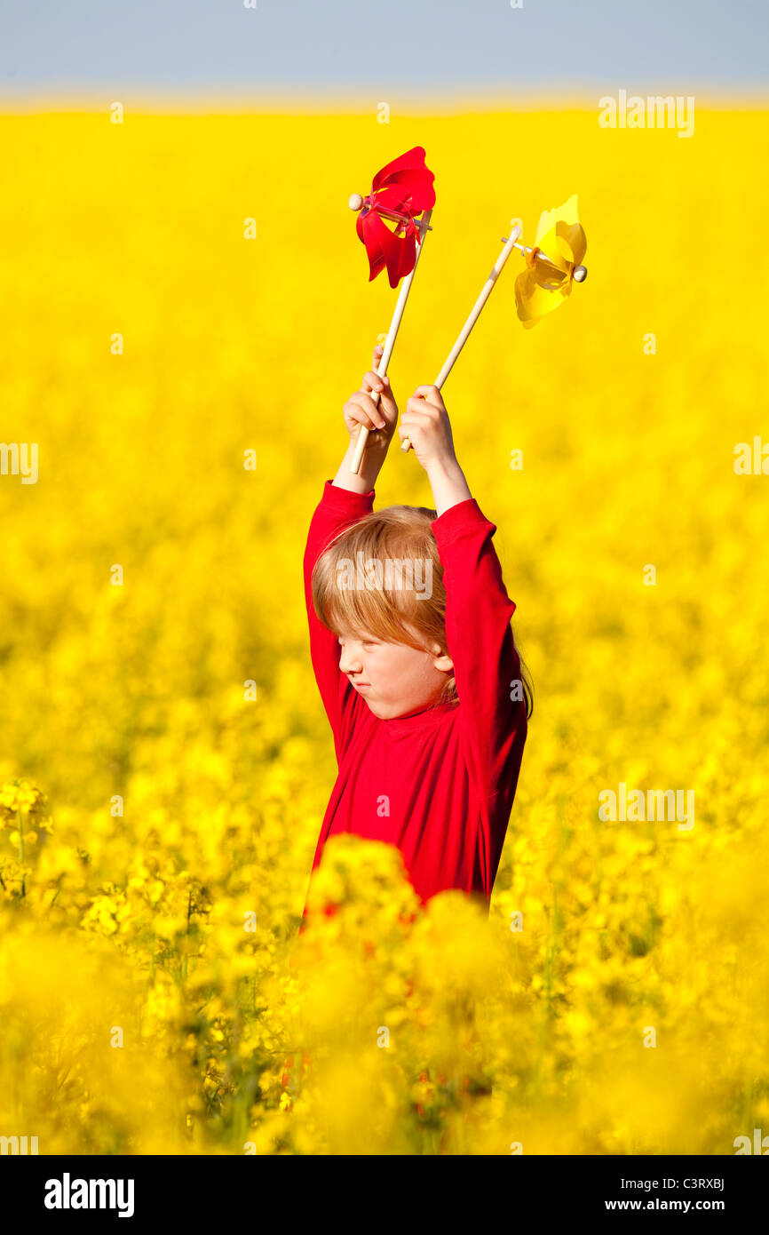 boy with long blond hair playing with pinwheels in canola field Stock ...