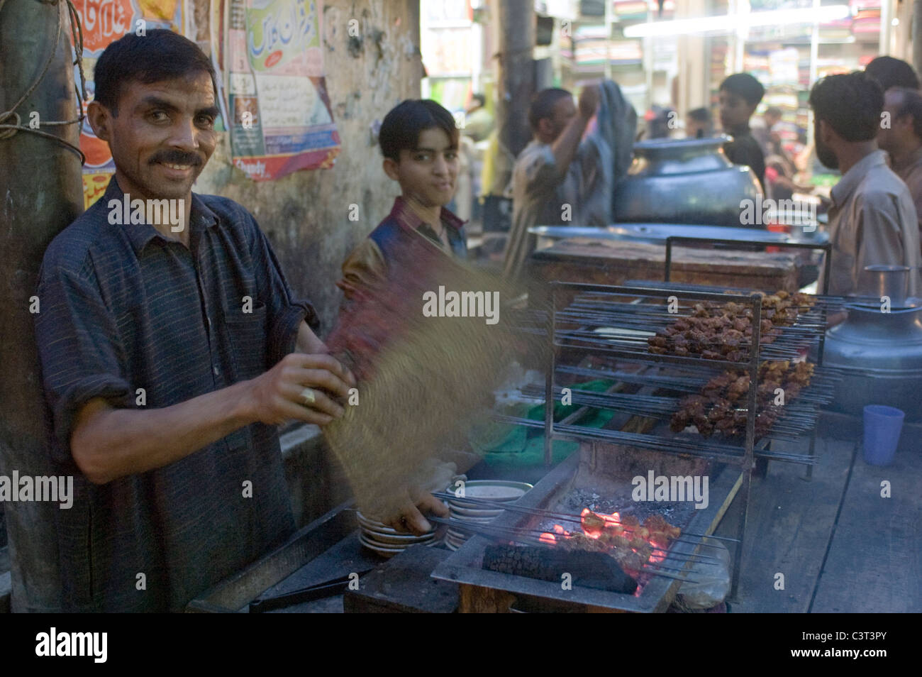 A man fans the coals while selling meat on a stick. Stock Photo