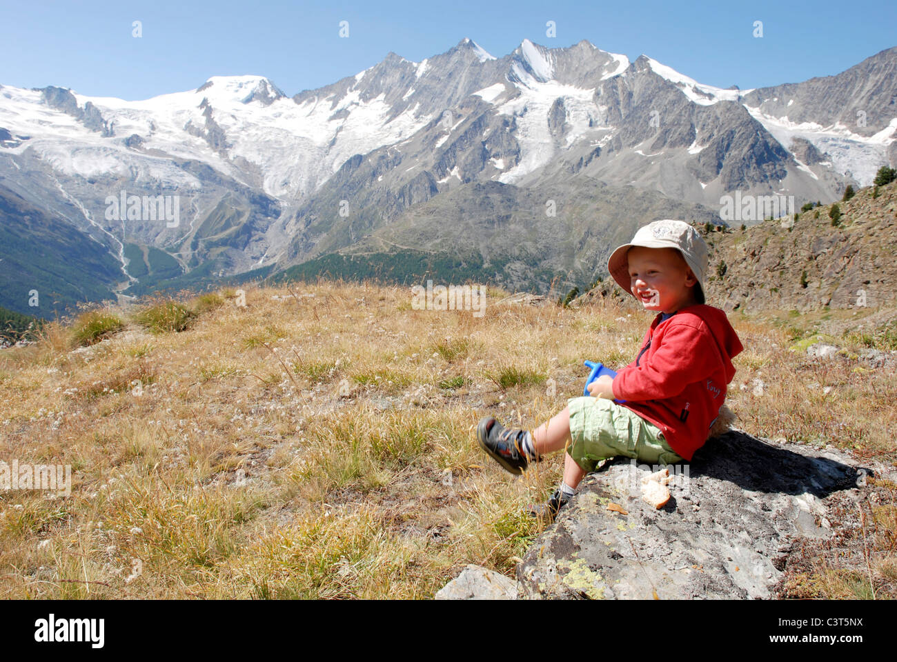 A young boy sat enjoying a drink and a picnic at Kreuzboden in the Saas valley, Switzerland. Stock Photo