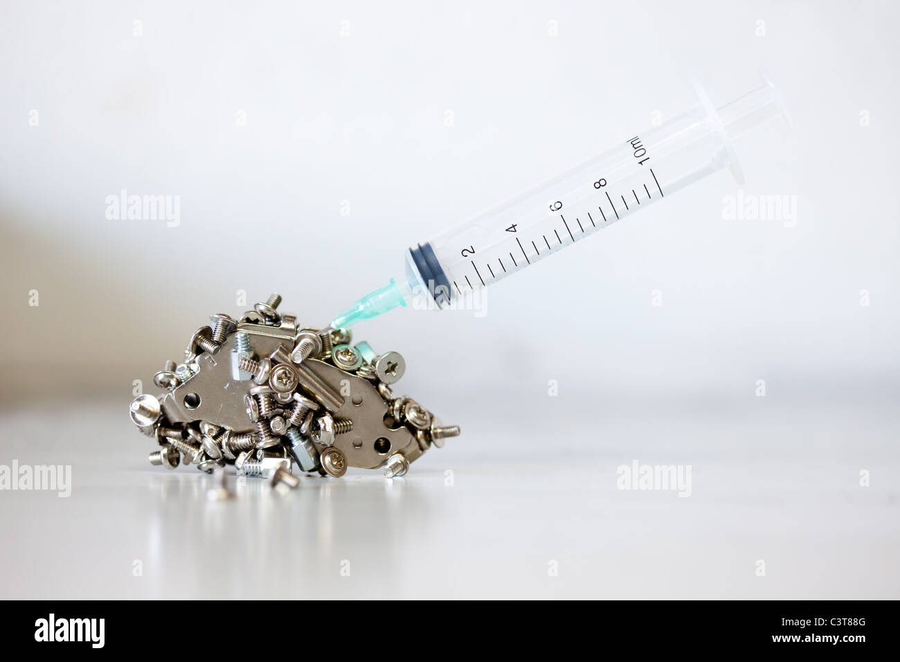 Syringe plunged into a pile of small computer nuts and bolts Stock Photo