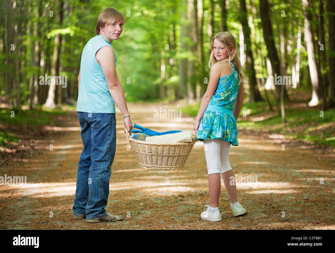 Teenager brother and sister walking along the path in the woods, carrying picnic basket Stock Photo