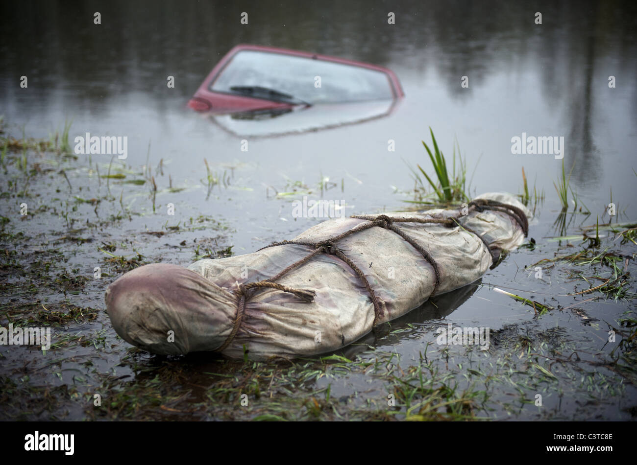A car half-sunken in a lake with a body bag in the foreground Stock Photo