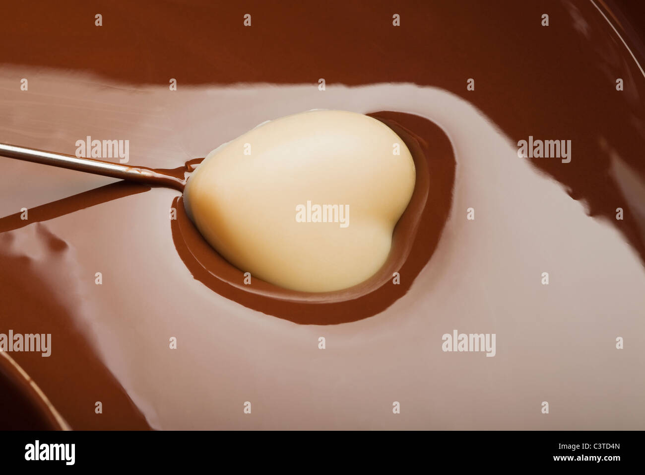 Heart-shaped candy being dipped in chocolate Stock Photo