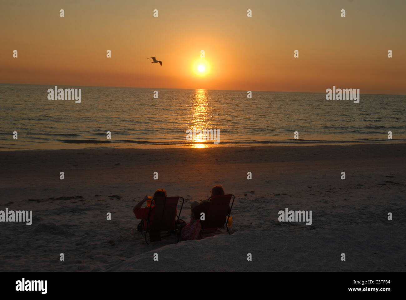 The sun sets as two people watch the sun set St. Pete Beach, Florida. Stock Photo