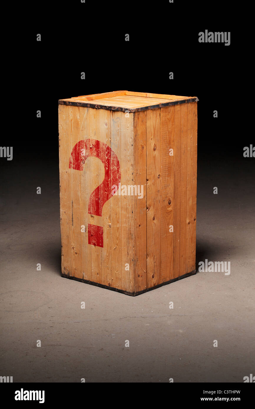 Old wooden crate with a photoshopped question mark on dirty concrete floor. Stock Photo