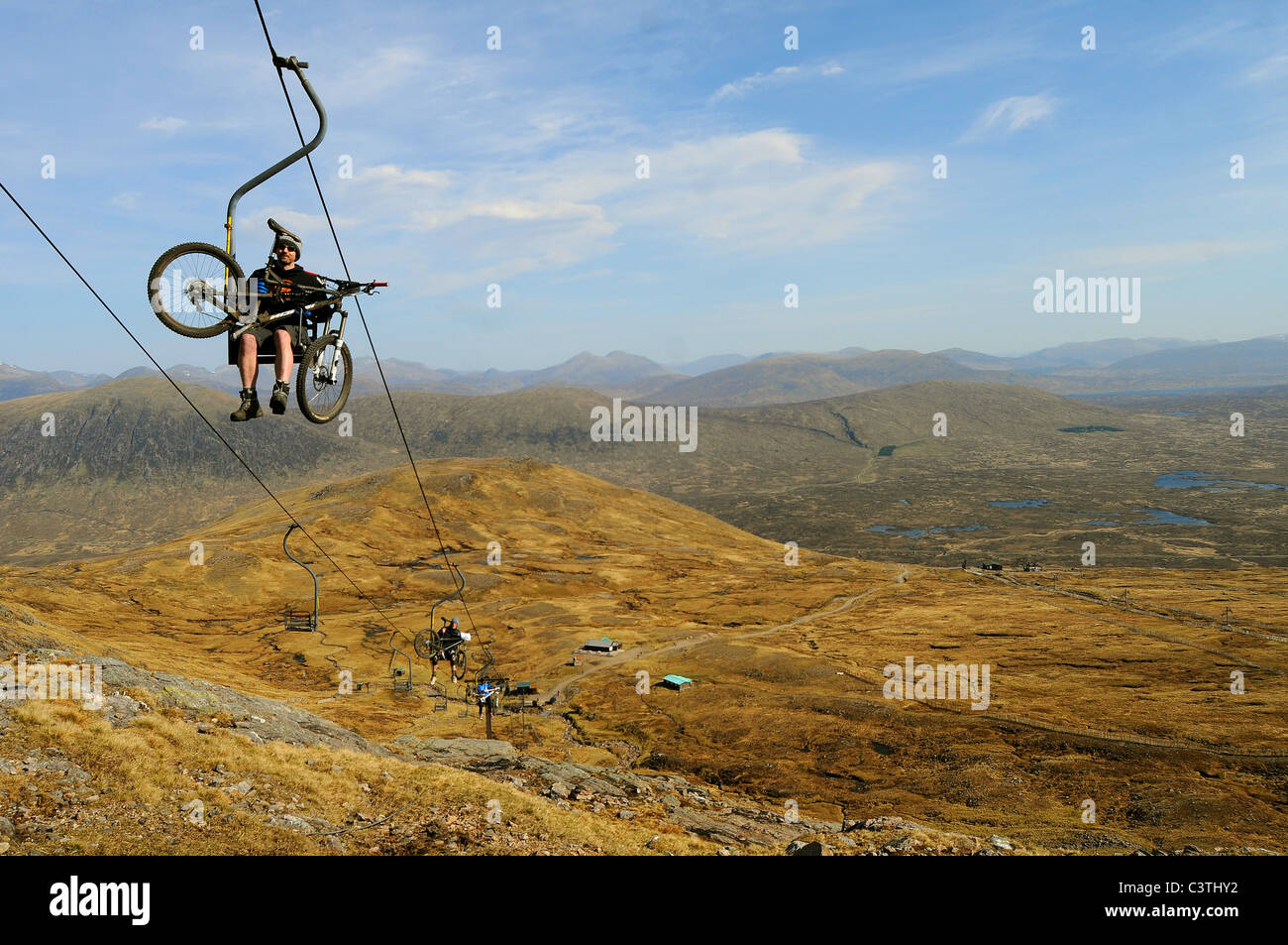 A mountain biker rides on the Cliffhanger single chairlift holding on ...