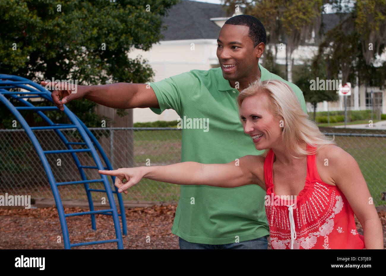 Mixed race couple at playground pointing something funny with children Stock Photo