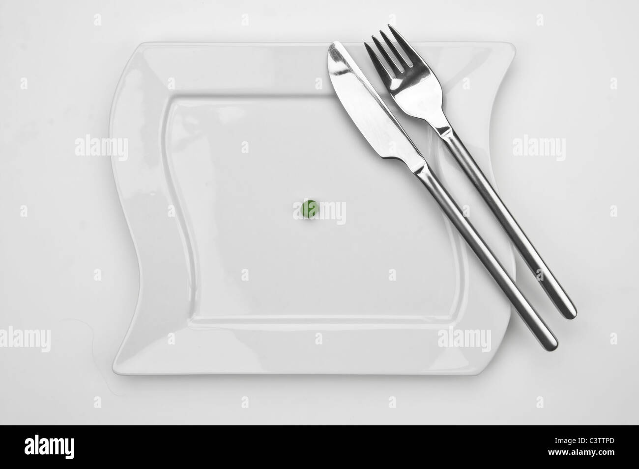 one pea on a white plate with fork and knife Stock Photo