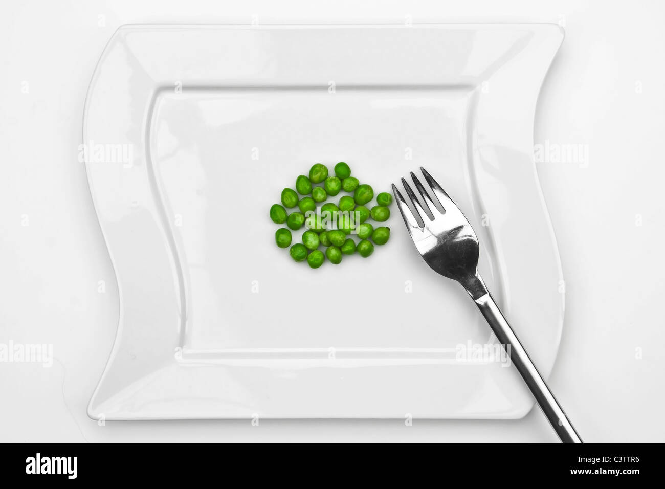 a bunch of peas on a white plate with a fork Stock Photo