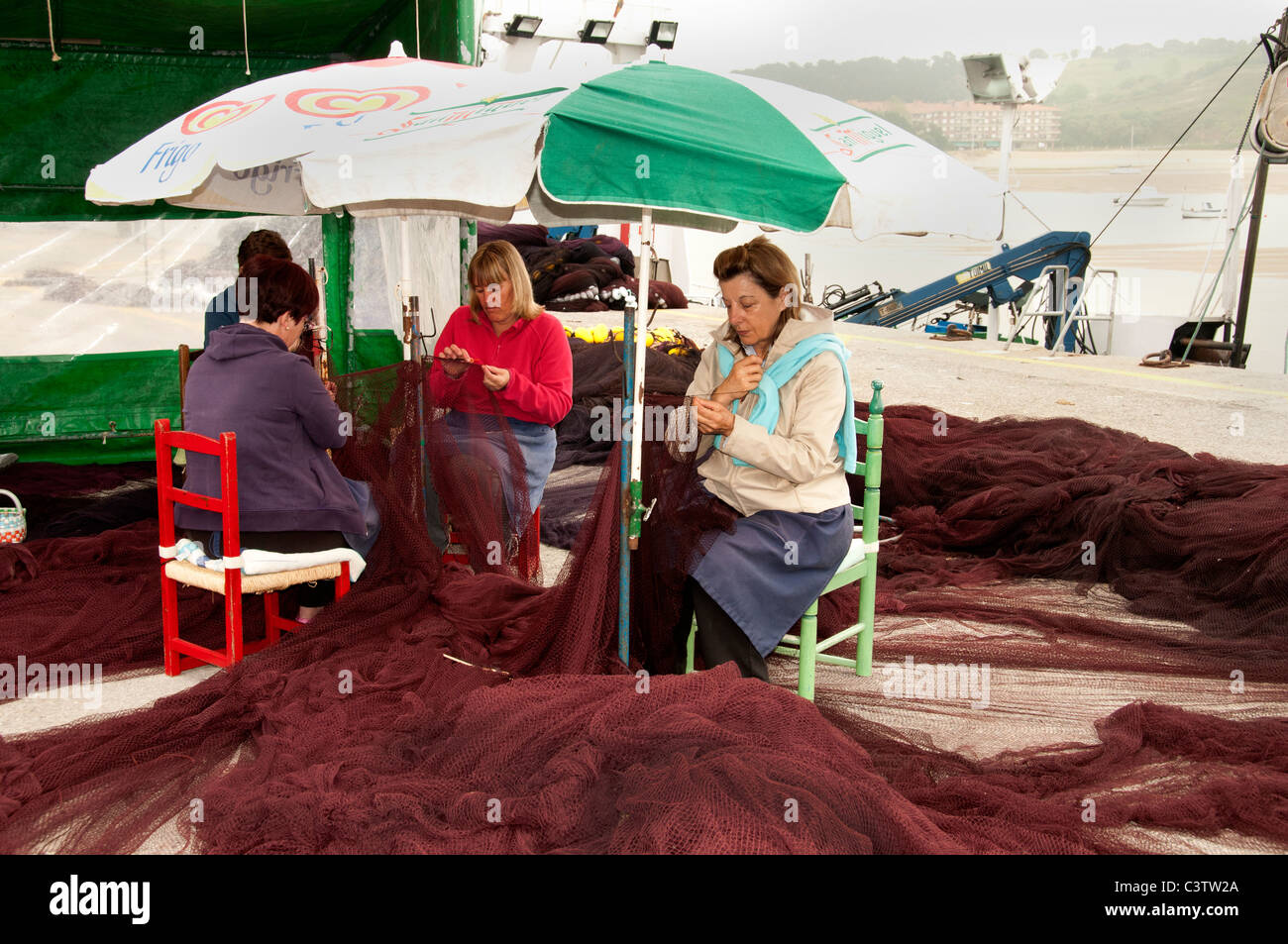 San Vicente de la Barquera Fishing port harbor Spain women woman  repairing sewing nets fines Stock Photo