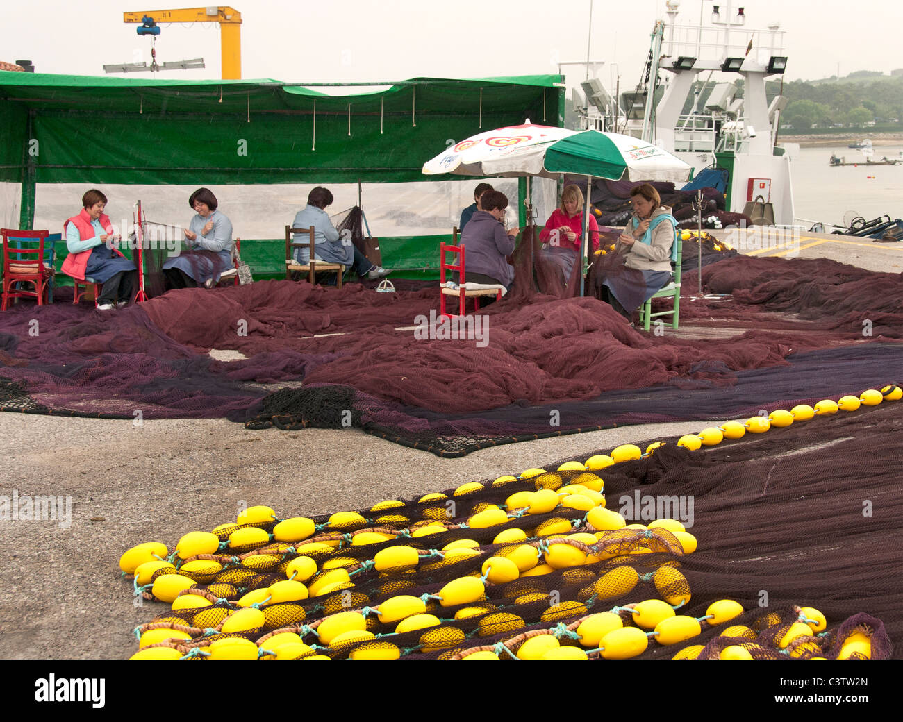 San Vicente de la Barquera Fishing port harbor Spain women woman  repairing sewing nets fines Stock Photo