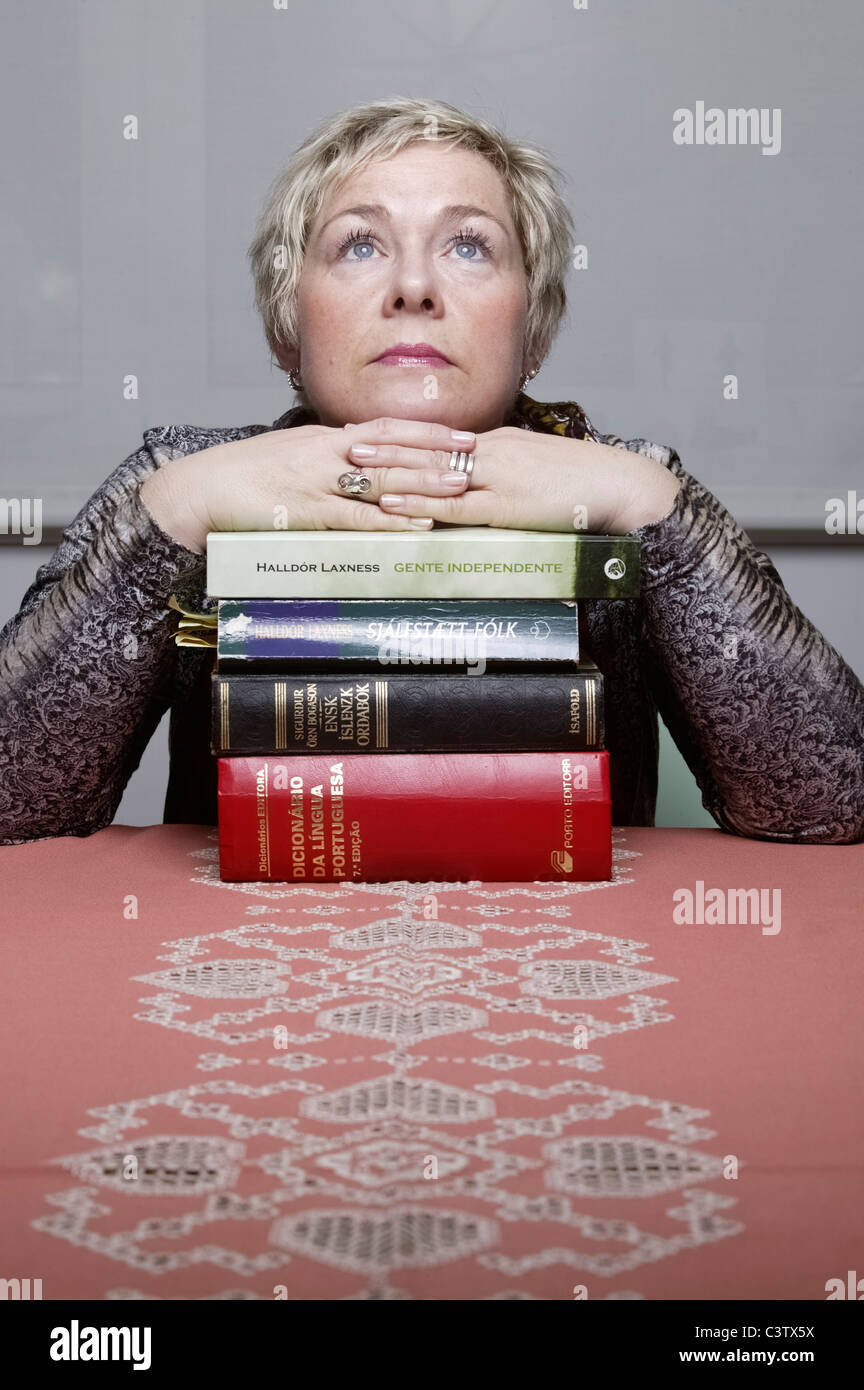 Portrait of blonde woman resting hands on top of pile of books looking up Stock Photo