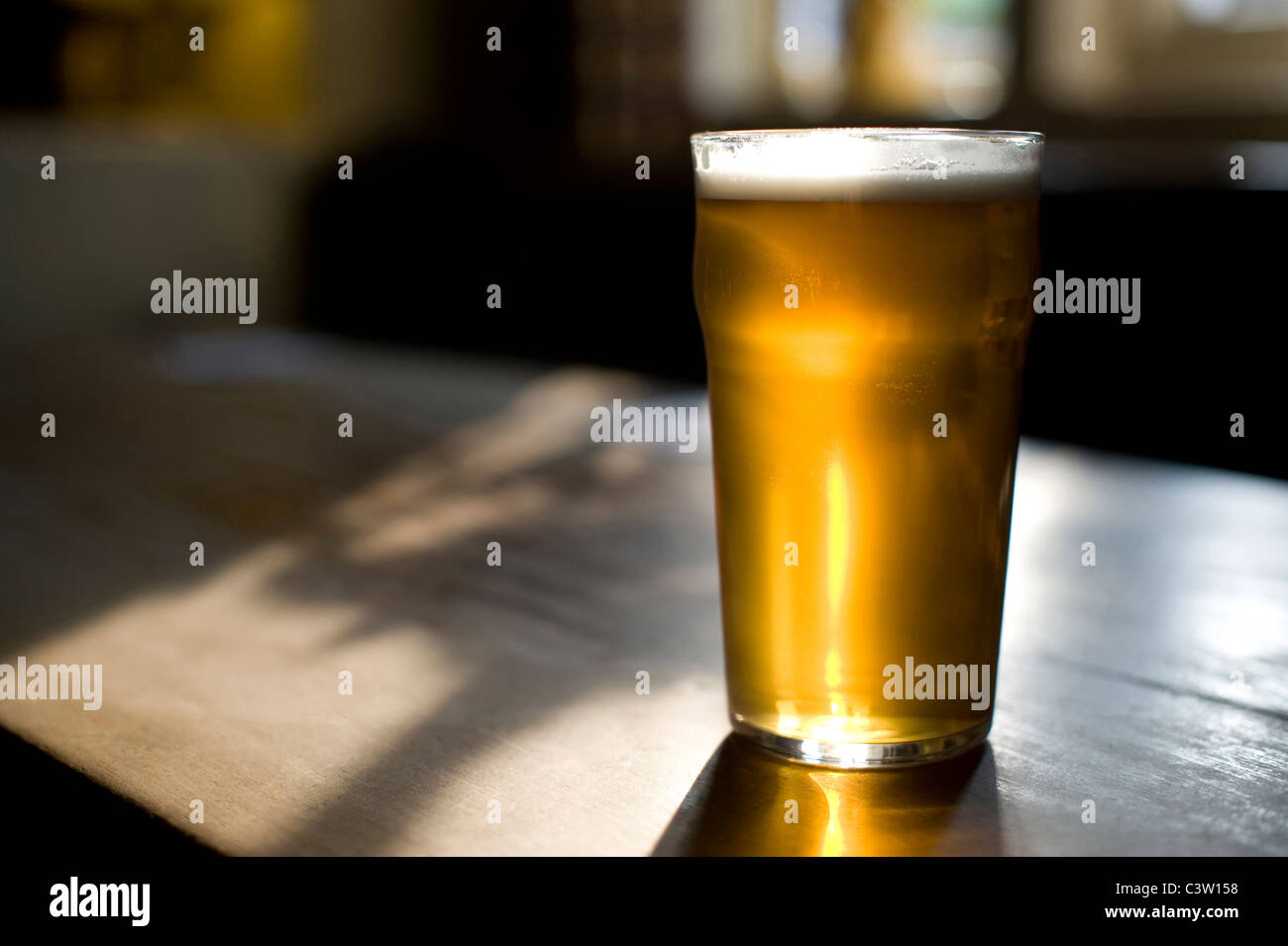 An almost full pint of real ale sits on a sunlit wooden table of a pub. Stock Photo