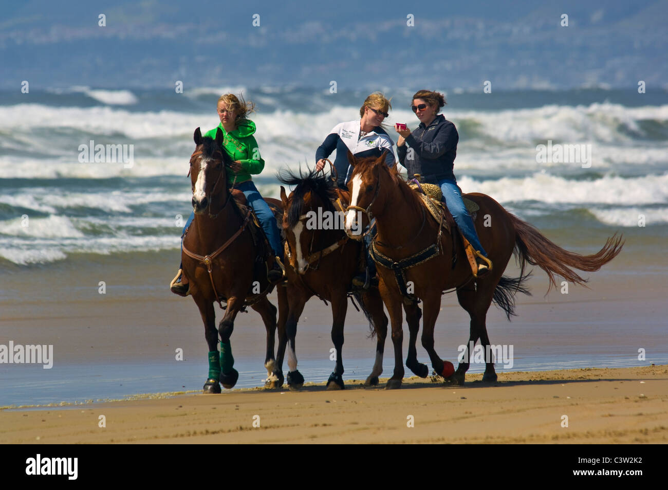 Three young women riding horses on the sand at Oceano State Beach, Oceano, California Stock Photo