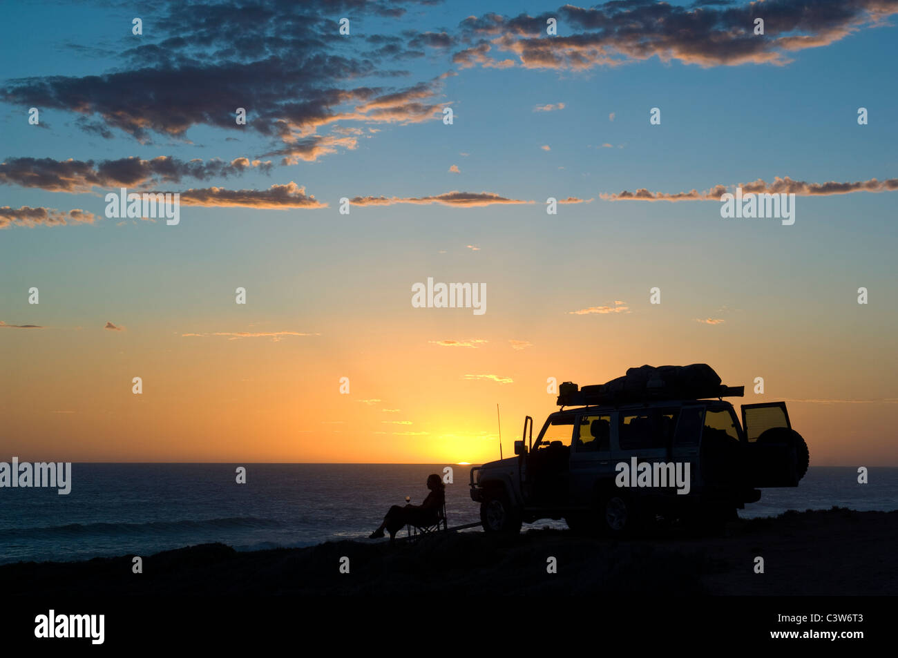 Woman with glass of wine by 4WD vehicle - sunset over the Southern Ocean. Nullarbor National Park, South Australia. Stock Photo