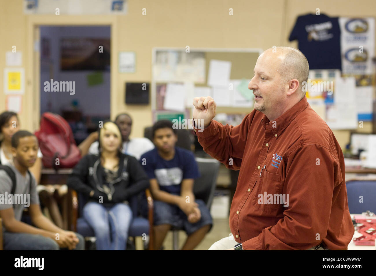 Male Anglo teacher talks to an ethnic and racial mix of students at