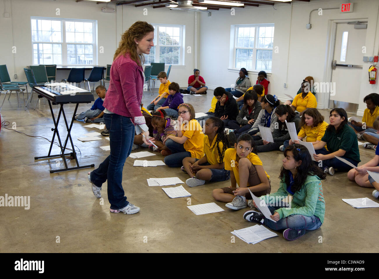 Middle school students look at sheet music before rehearsing song during music class taught by Anglo female teacher. Stock Photo