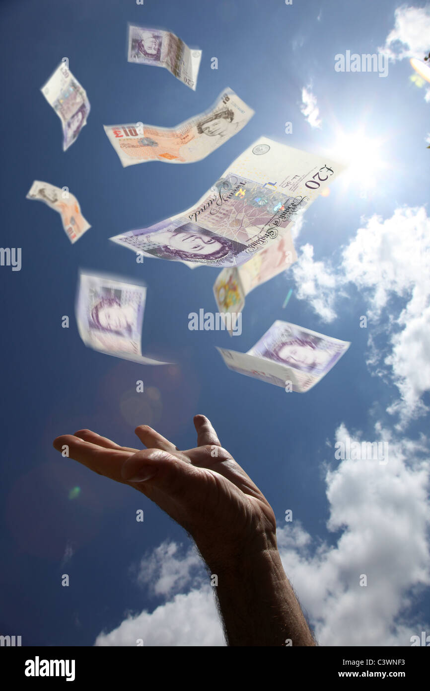 £10 and £20 notes falling from the sky, a male hand reaching up to catch the money. Stock Photo