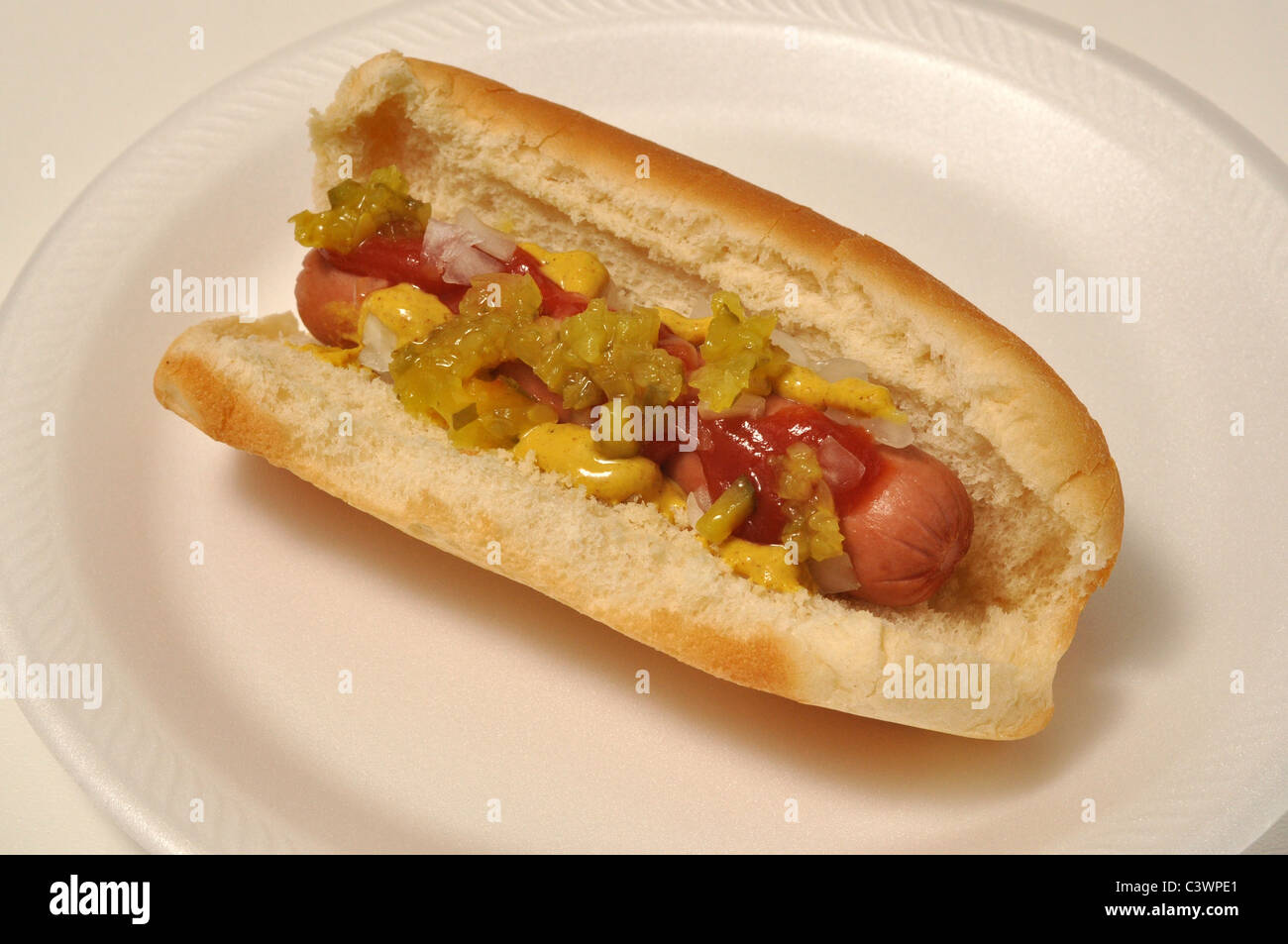 A hot dog with all the works is on a white plate. Stock Photo