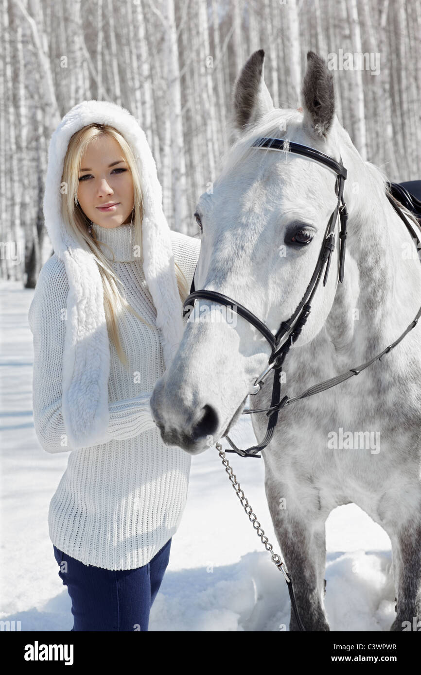 outdoor portrait of beautiful blonde girl with pale horse in sunny winter forest Stock Photo
