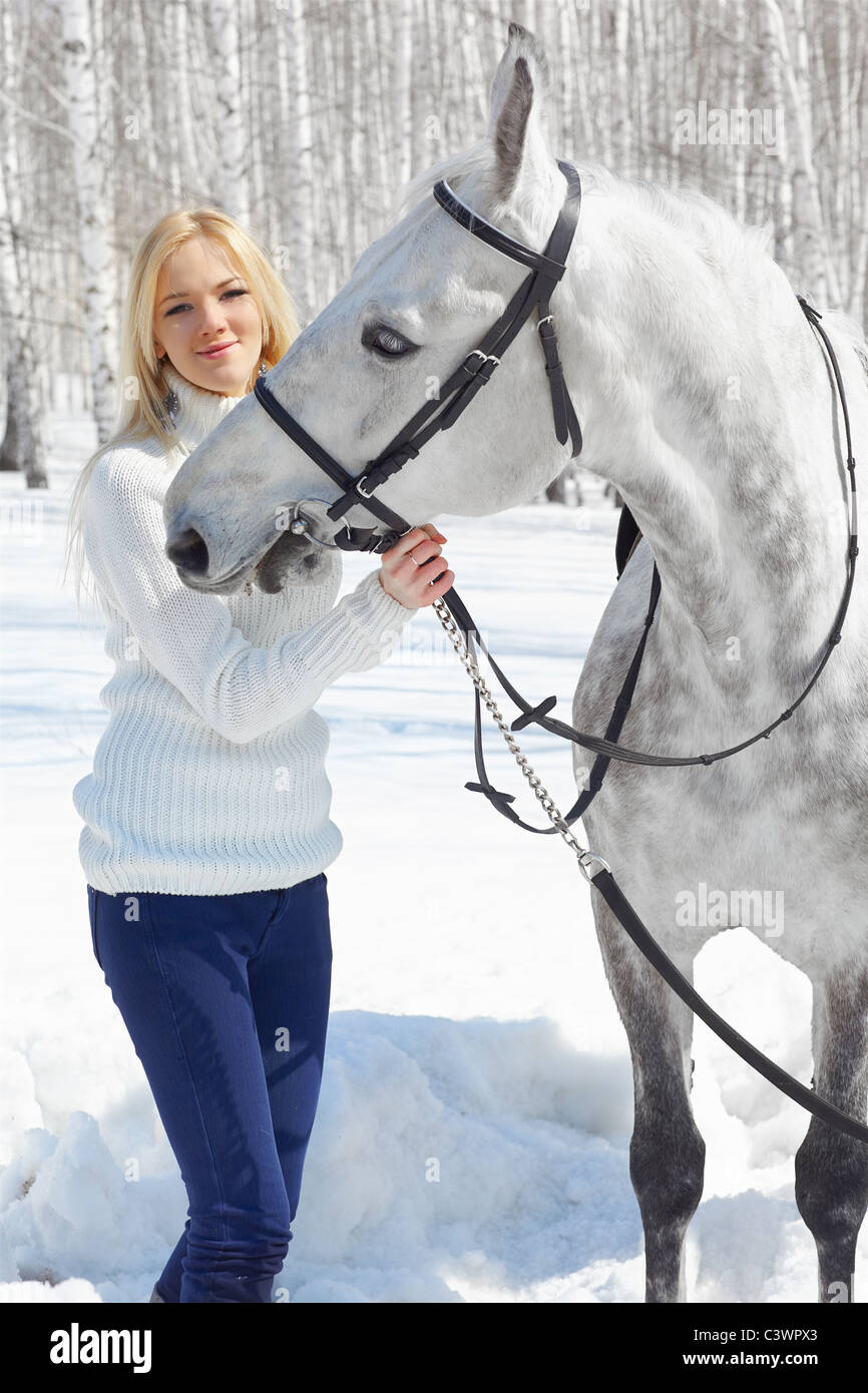outdoor portrait of beautiful blonde girl with pale horse in sunny winter forest Stock Photo