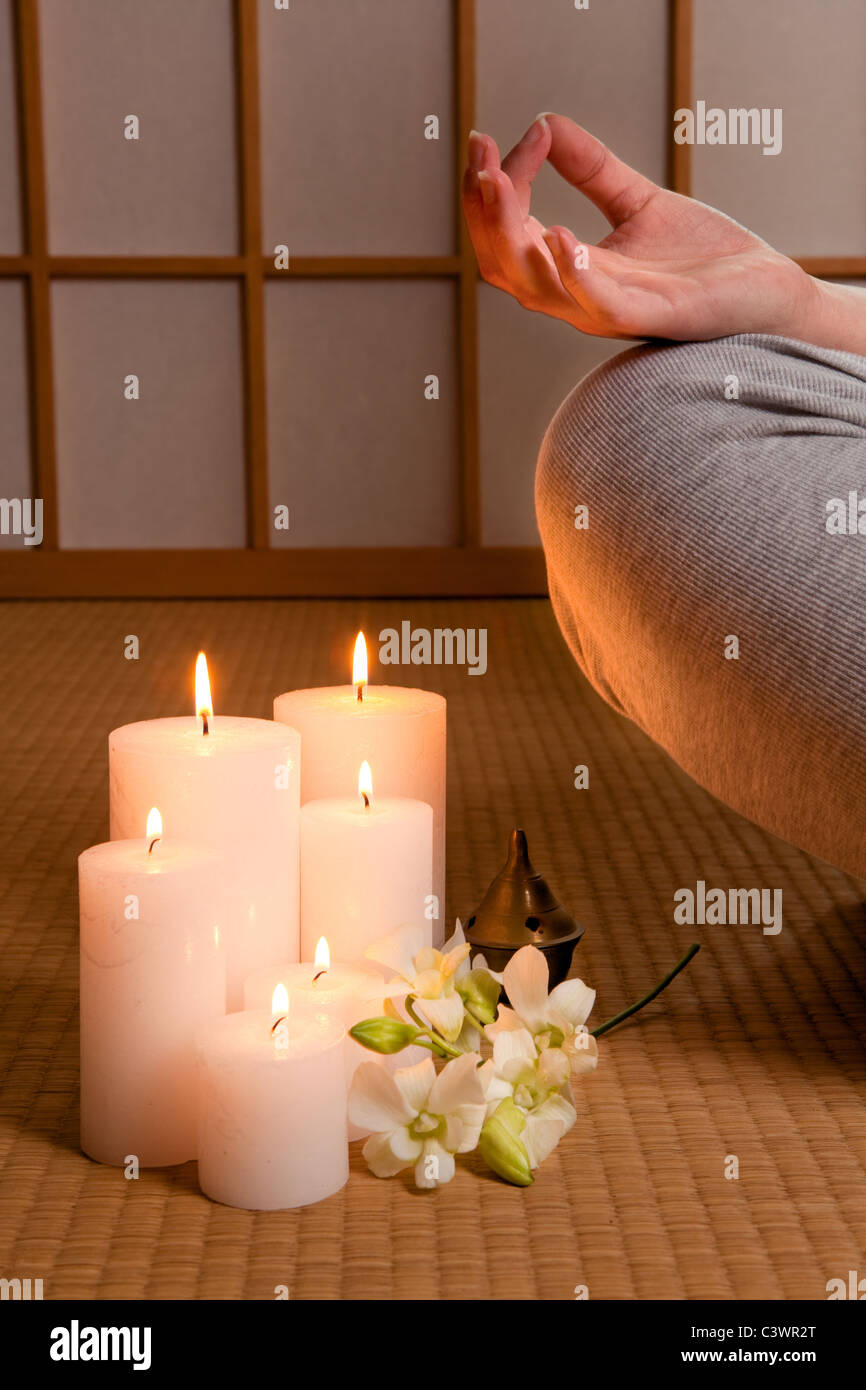 Meditating woman on japanese tatami mat with candles and orchids Stock Photo