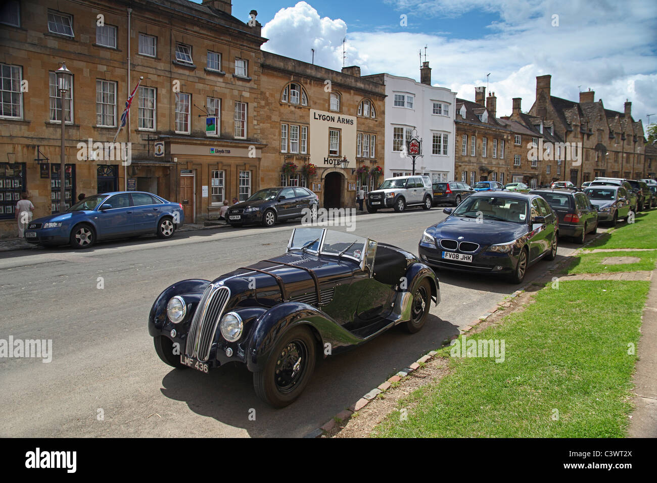 A vintage BMW 328 car parked in front of a modern BMW car in the High Street of Chipping Campden, Gloucestershire, England, UK Stock Photo