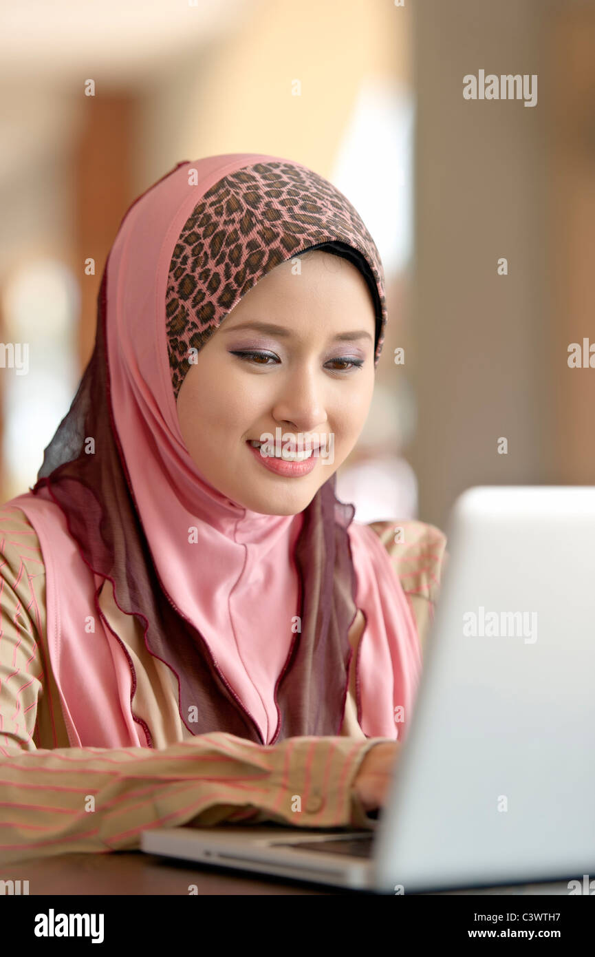 Young pretty Asian muslim woman concentrates working with laptop in ...