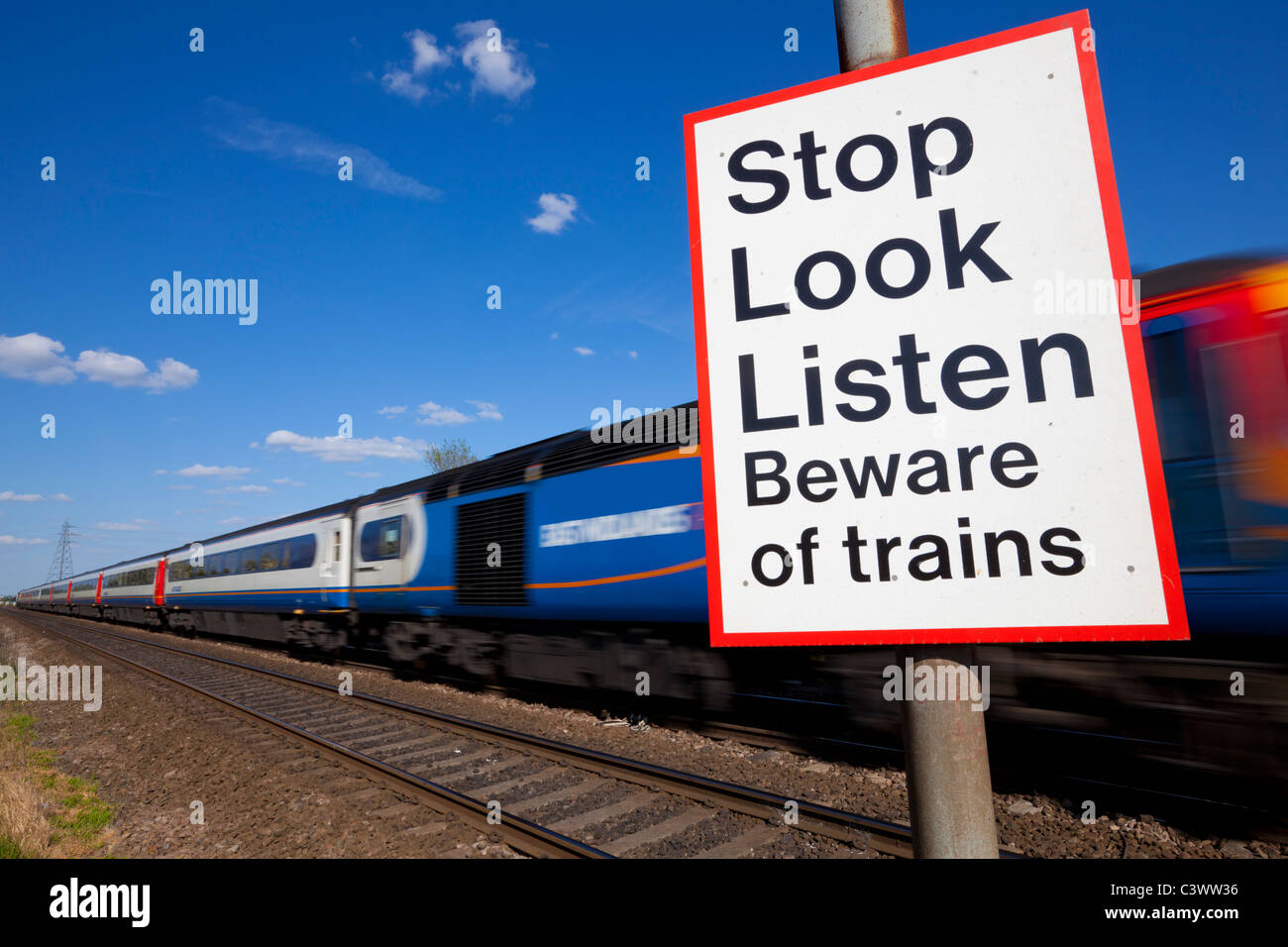 Stop look listen beware of trains sign by a Speeding train passing a railway crossing warning sign  England GB UK Europe Stock Photo