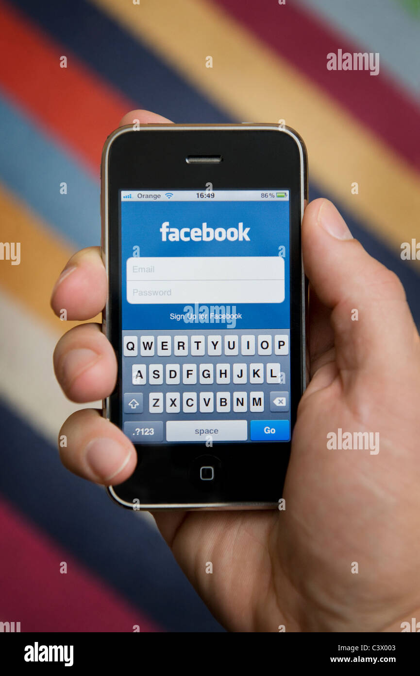 Close up of male hand holding an Apple iPhone about to log in to Facebook. (Editorial use only). Stock Photo
