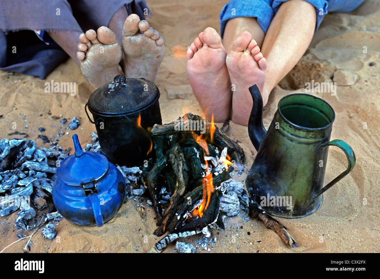 Algeria, Djanet, Sahara Desert, Feet of man of Tuareg tribe and tourist. Tea pots. Campfire. Stock Photo