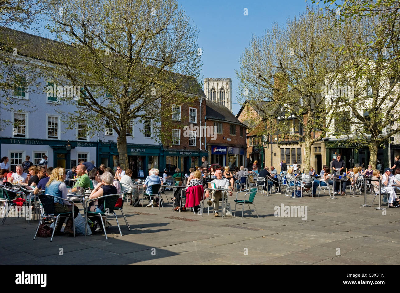 People tourists visitors sitting outside at pavement cafes in spring St Sampsons Square York North Yorkshire England UK United Kingdom Great Britain Stock Photo