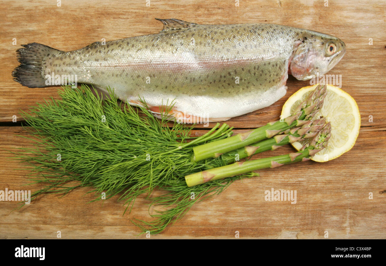 Fresh rainbow trout with dill, asparagus and lemon on old weathered wood Stock Photo