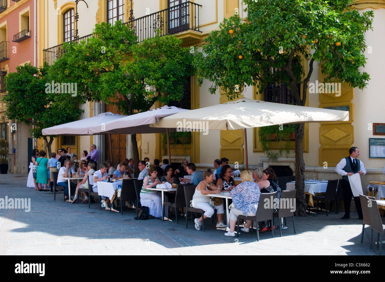 Street scene, Seville, Spain. People enjoying eating and drinking at an outdoor cafe bar with parasols. Stock Photo