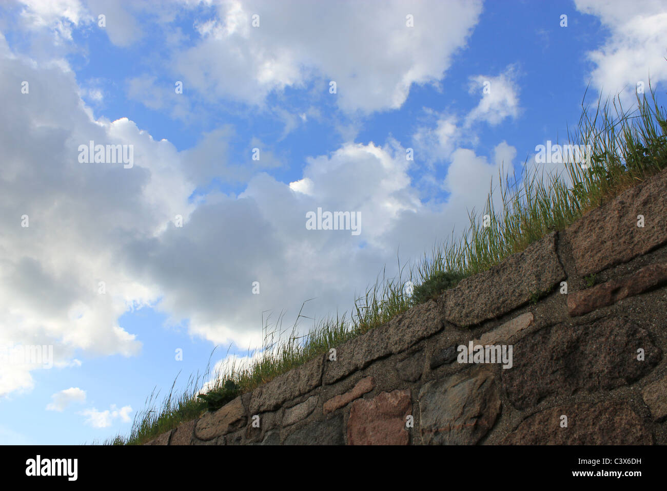 Blue sky with clouds and grass growing on stone fence Stock Photo - Alamy