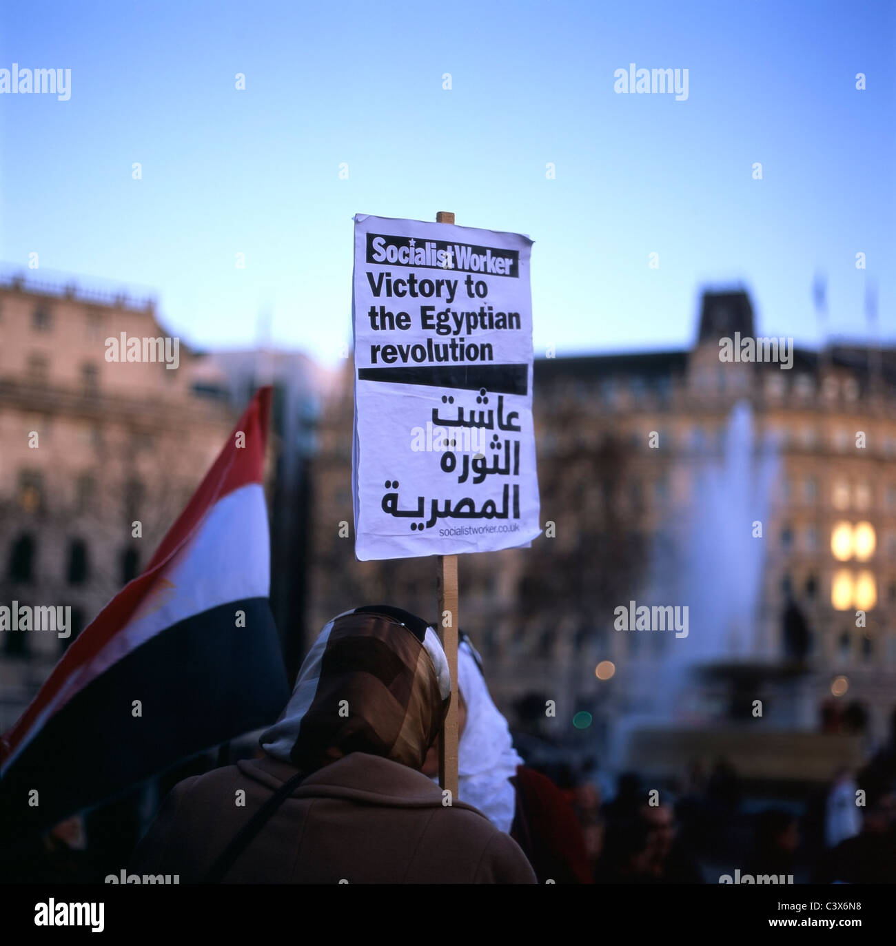 Egyptians woman (back rear view) female supporter wearing headscarf standing at demonstration in Trafalgar Square holding an Arabic and English language Socialist Worker poster supporting Victory to the Egyptian Revolution during the Arab Spring uprising in Egypt, London UK  2011  KATHY DEWITT Stock Photo