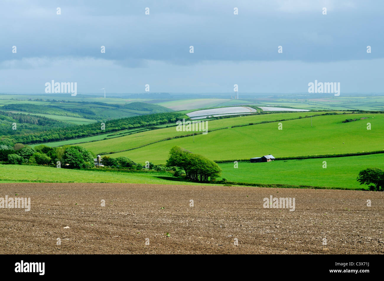 A ploughed field and the rolling hills of North Devon with new wind turbines being erected in the distance. Woolacombe, Devon, England. Stock Photo