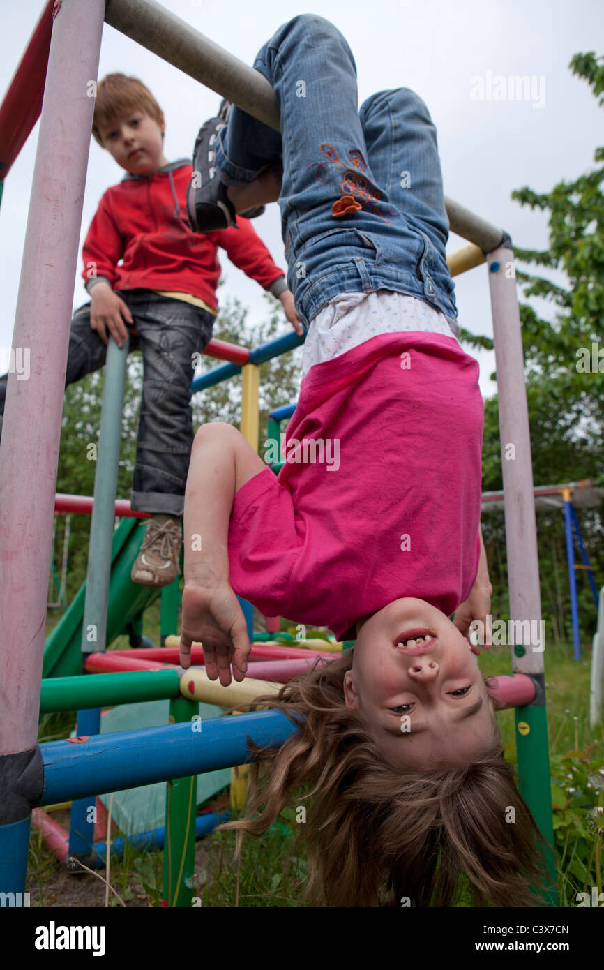 little girl hanging down monkey bars, her brother watching Stock Photo