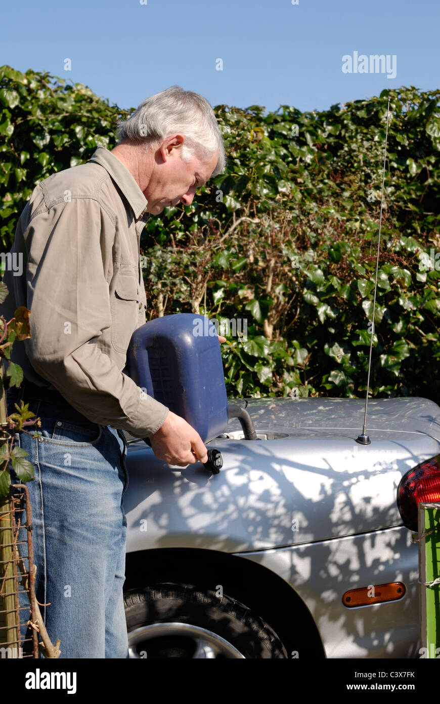 Mature man putting fuel into vehicle from a carry can in a rural environment Stock Photo