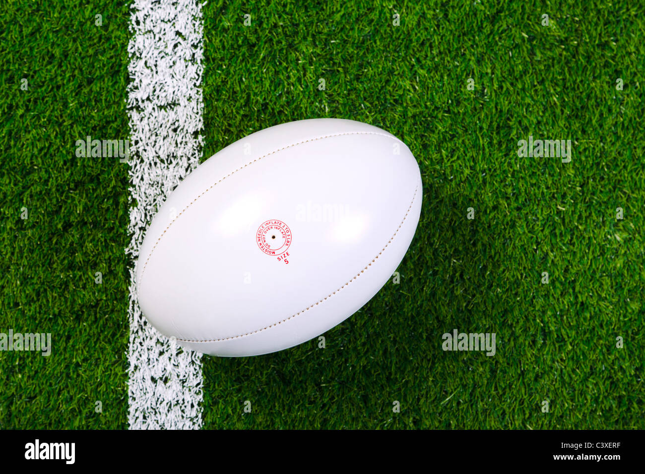 Photo of a rugby ball on a grass next to the white line, shot from above. Stock Photo