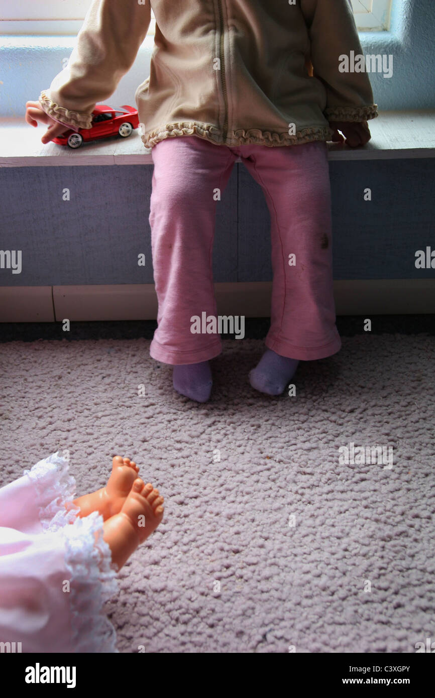 A little girl holding a toy car while a doll lays on the ground at her feet. Stock Photo
